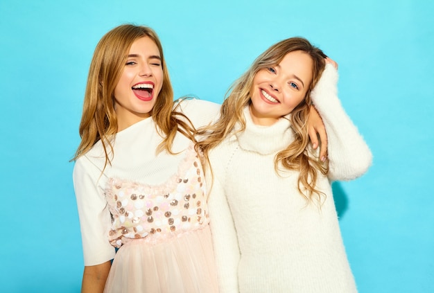 Free photo two young beautiful smiling hipster women in trendy summer white clothes. sexy carefree women posing near blue wall. positive models