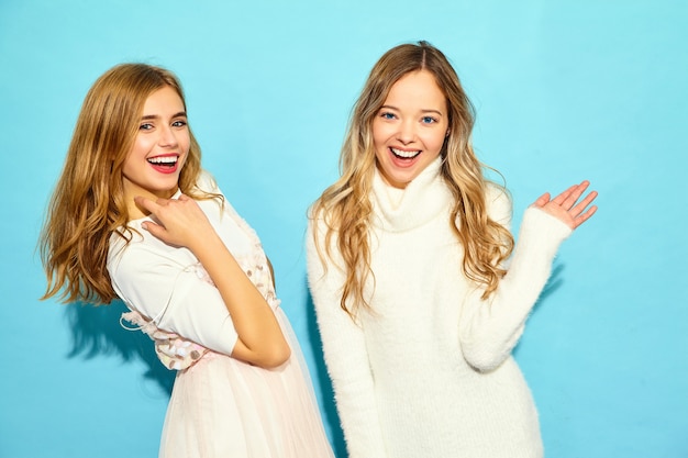 Free photo two young beautiful smiling hipster women in trendy summer white clothes. sexy carefree women posing near blue wall. positive models