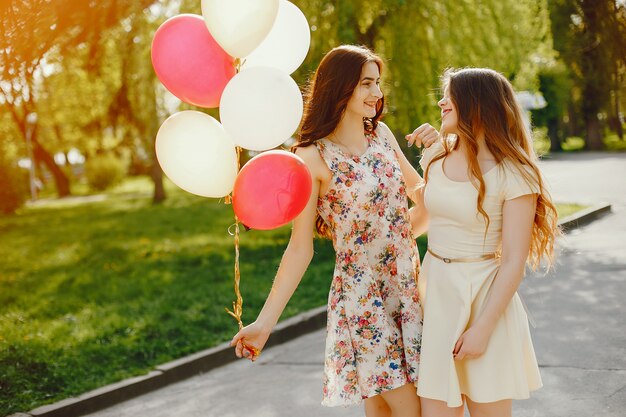 two young and bright girls spend their time in the summer park with balloons