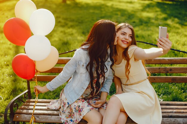 two young and bright girls spend their time in the summer park with balloons