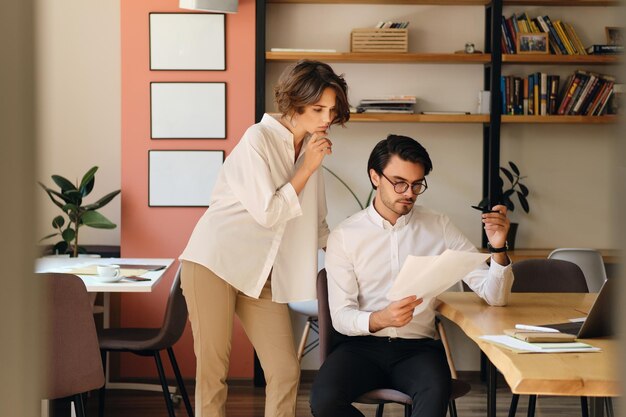 Two young business colleagues thoughtfully working with papers in modern office