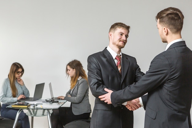 Free photo two young businessmen shaking hands during meeting in office