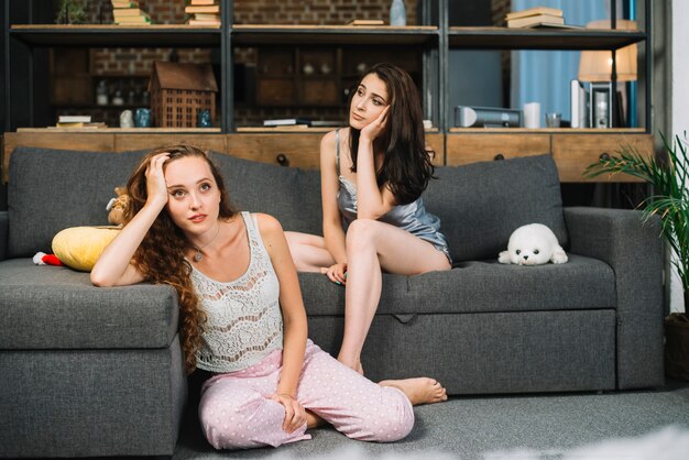 Two young contemplated women sitting at home