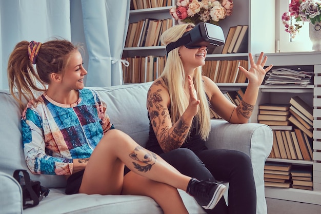 Two young girlfriends in casual clothes having fun with virtual reality glasses device at home.