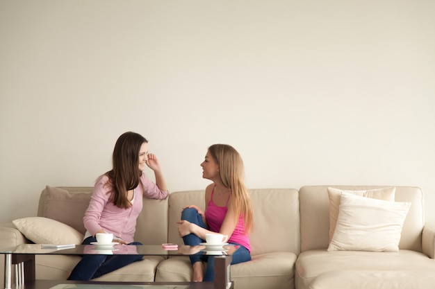 Two young girlfriends relaxing at home and having personal conversation