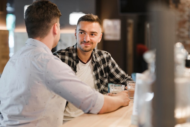 Free Photo two young male friends enjoying glasses of drink