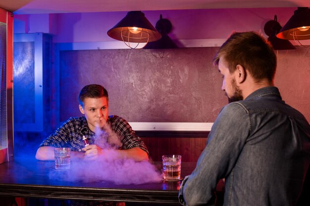 Two young men smoke electronic cigarettes in a vapebar. Vape shop