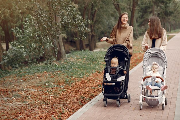 Two young mothers walking in a autumn park with carriages