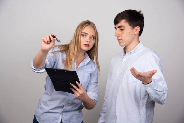 Two young office colleagues discussing a project on gray wall.