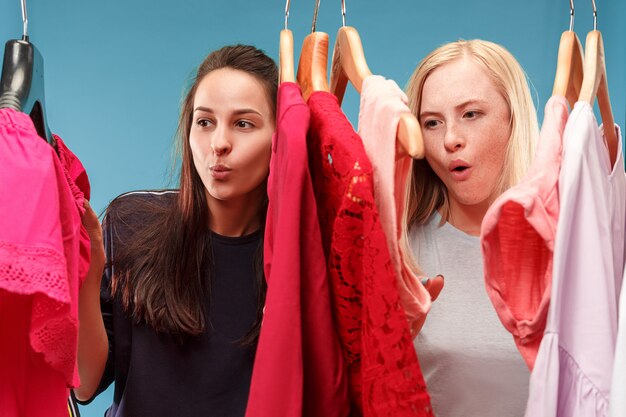 The two young pretty girls looking at dresses and try on it while choosing at shop