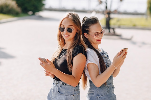 Two young pretty girls on a walk in the park with phones