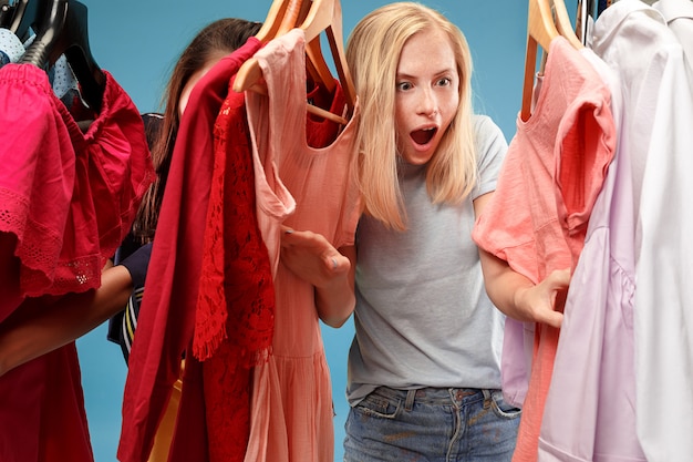 The two young pretty women looking at dresses and try on it while choosing at shop