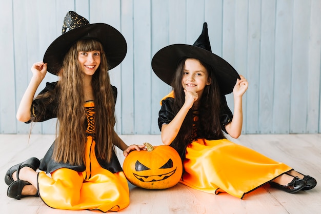 Two young witches smiling and sitting on floor on Halloween