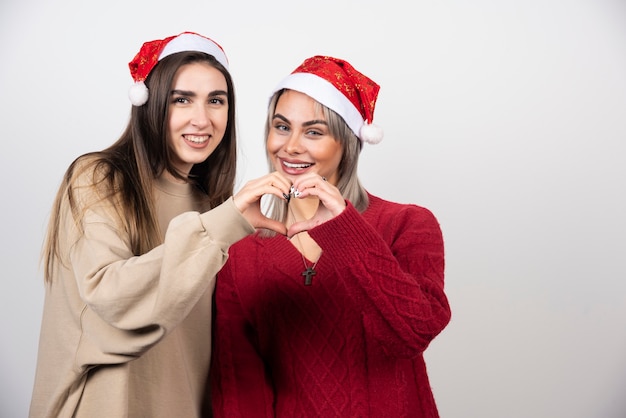 Two young women doing heart symbol gesture and laughing .