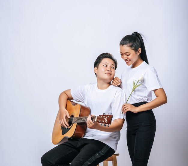 Two young women sat on a chair and played guitar.