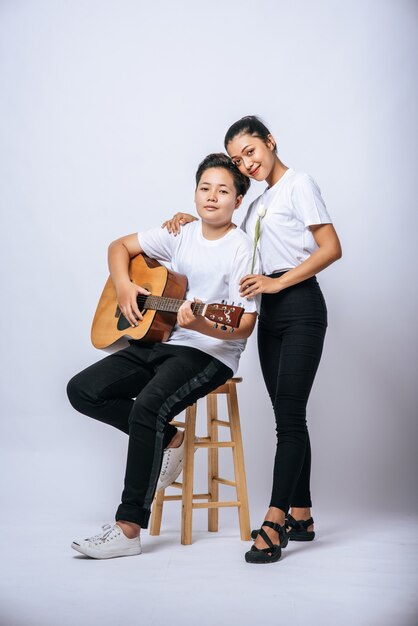 Two young women sat on a chair and played guitar.