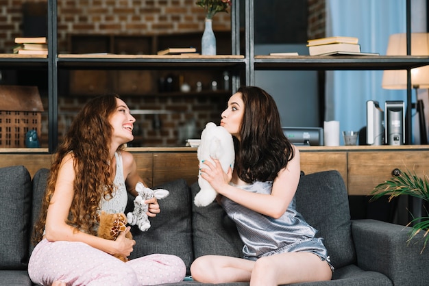 Two young women sitting on sofa holding soft toy