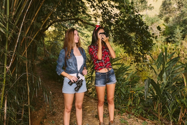 Free photo two young women standing in forest clicking photograph with camera