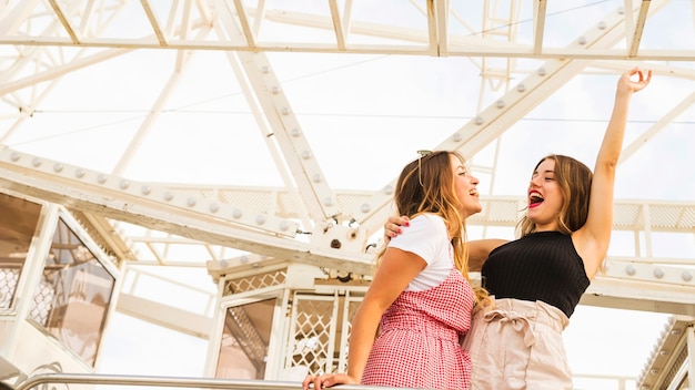 Two young women standing in front of ferris wheel making fun