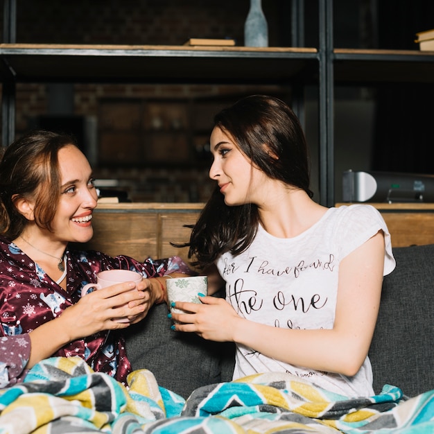 Free photo two young women with cup of coffee looking at each other