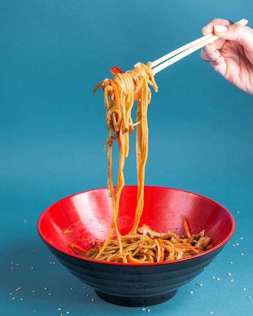 udon stir fried noodles with bell pepper carrot spring onion soy sauce and sesame in a bowl