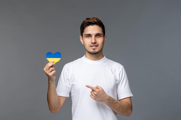 Free photo ukraine russian conflict cute handsome guy in white shirt with ukrainian heart smiling