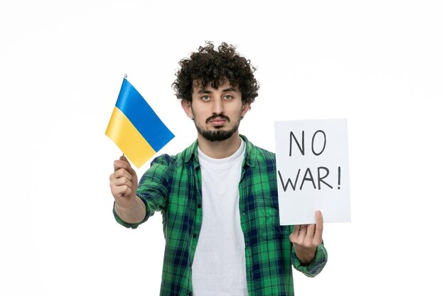 Ukraine russian conflict cute young brunette guy in green shirt holding no war sign ukrainian flag