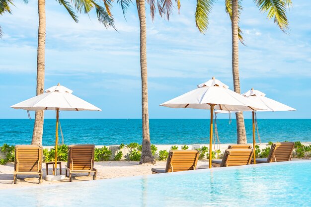 Umbrella and deck chair around outdoor swimming pool in hotel resort with sea ocean beach and coconut palm tree