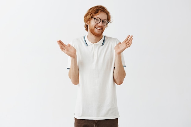 Free photo unbothered bearded redhead guy posing against the white wall with glasses