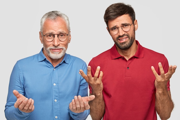 Free photo uncertain father and young adult son posing against the white wall