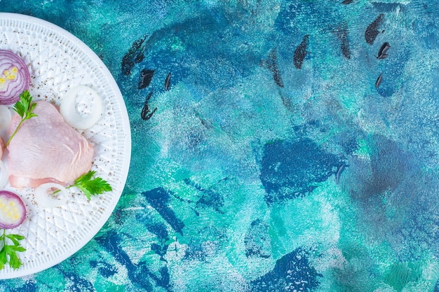 Uncooked chicken hip with onion rings and parsley on a plate