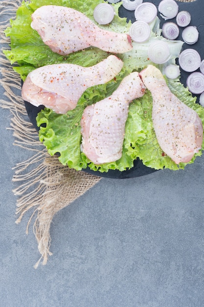 Free photo uncooked chicken legs and sliced onion on black board.