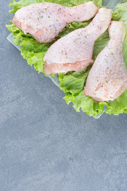 Uncooked chicken legs with lettuce on wooden board.