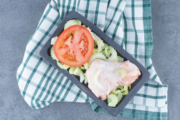 Uncooked chicken wings and tomato on black plate.