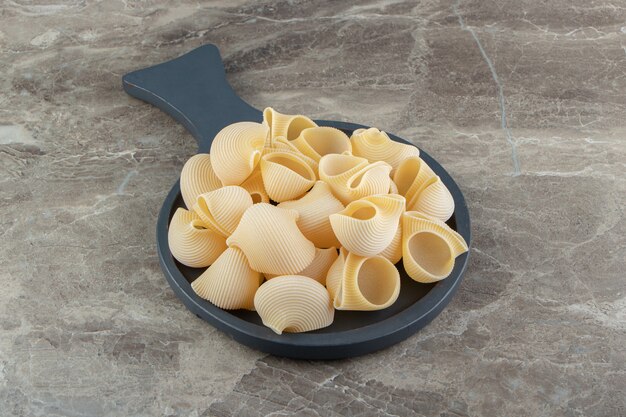 Uncooked conchiglie pasta on black board.