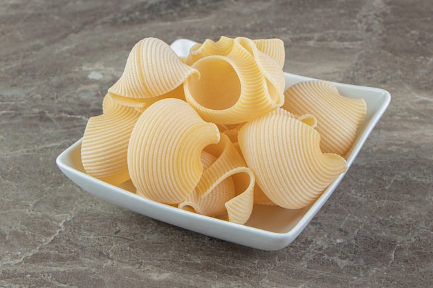 Uncooked conchiglie pasta in white bowl