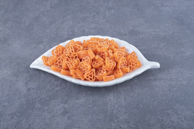 Uncooked heart-shaped pasta on leaf-shaped plate.