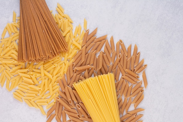 Uncooked macaroni with fresh raw pasta on white surface