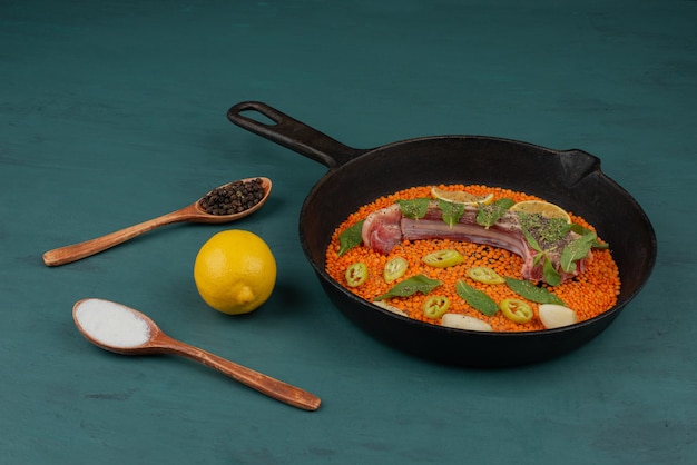 Free Photo uncooked meat with red lentil, pepper slices, garlic and spinach in black pan with lemon and spices.