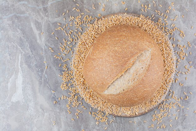 Uncooked oat grains with loaf of bread on marble surface