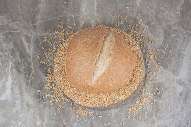 Uncooked oat grains with loaf of bread on marble surface