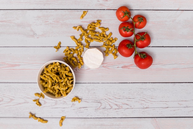 Free photo uncooked pasta; red tomatoes and closed container over wooden table