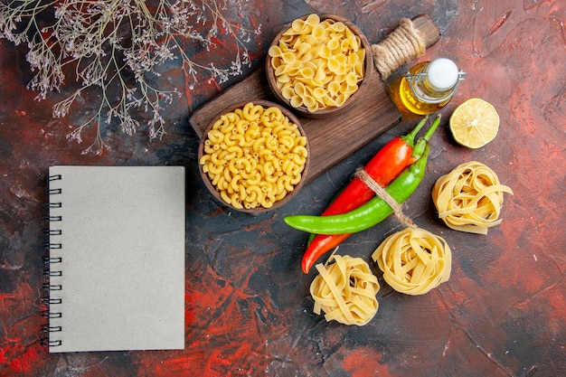 Free photo uncooked pastas cayenne peppers tied in one another with rope oil bottle lemon garlic and notebook on mixed color table