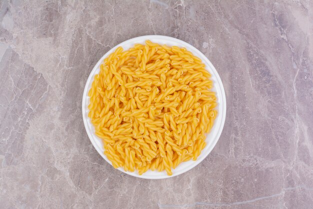 Uncooked pastas in a white ceramic cup on the marble. 