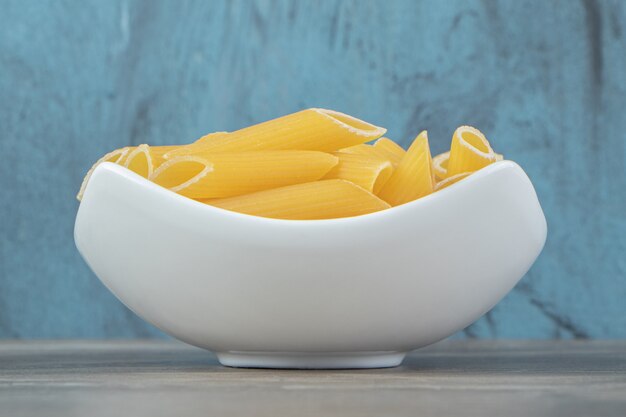 Uncooked penne pasta in white bowl.