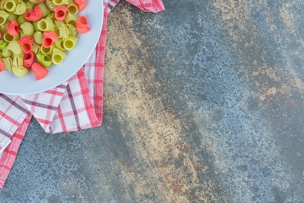 Free photo uncooked pipe rigate pasta in plate on the tea towel, on the marble surface.