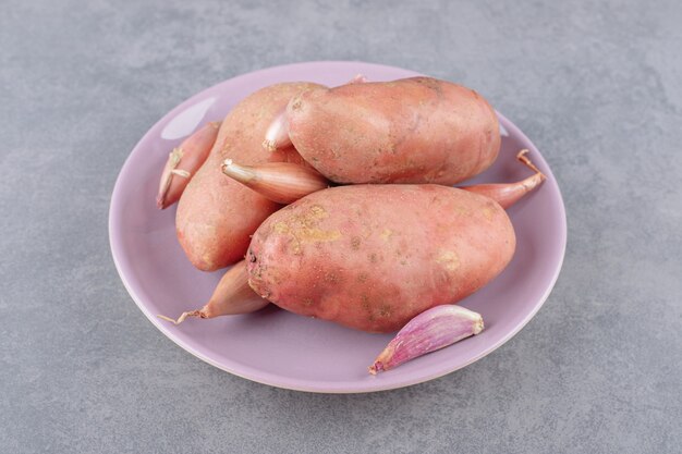 Uncooked potatoes with garlics in a purple plate . 