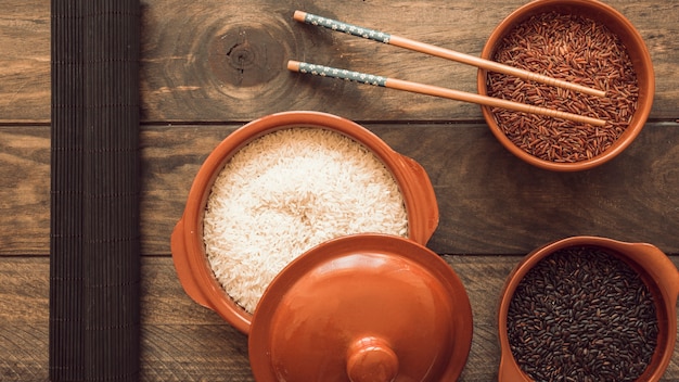 Uncooked rice grains bowls with chopsticks on wooden table