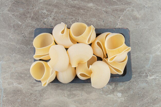 Uncooked seashell pasta on black plate.