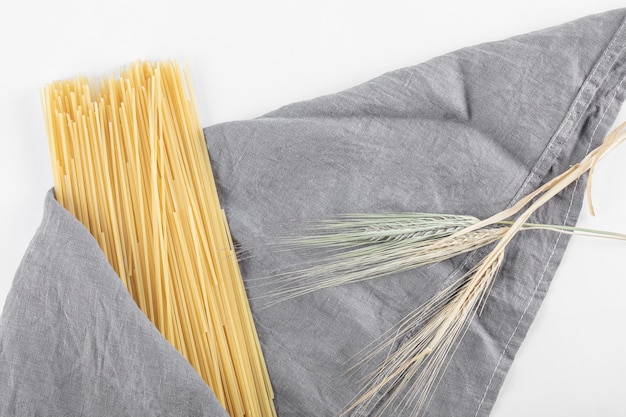 Uncooked spaghetti pasta on gray tablecloth with wheat.